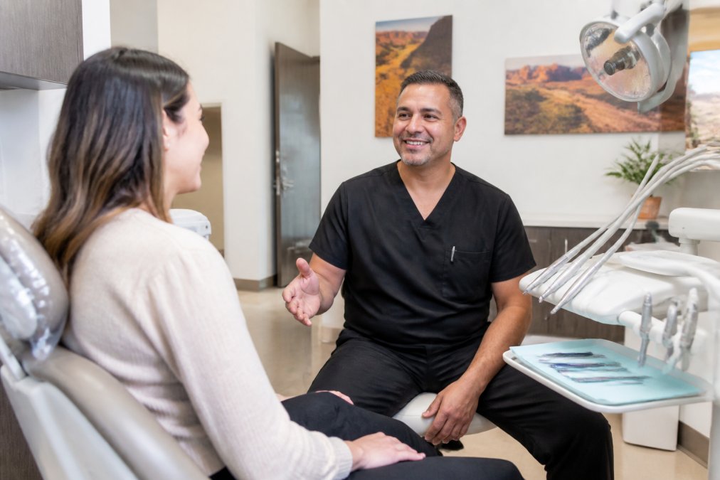 A friendly dentist in a modern, bright office welcoming an adult patient into the examination room for a routine check-up