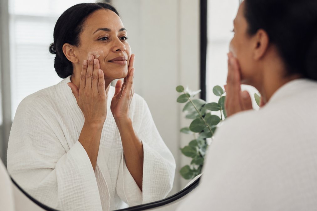 Woman's hands gently applying moisturizer to her face in soft natural light, showing a calm, caring skincare moment