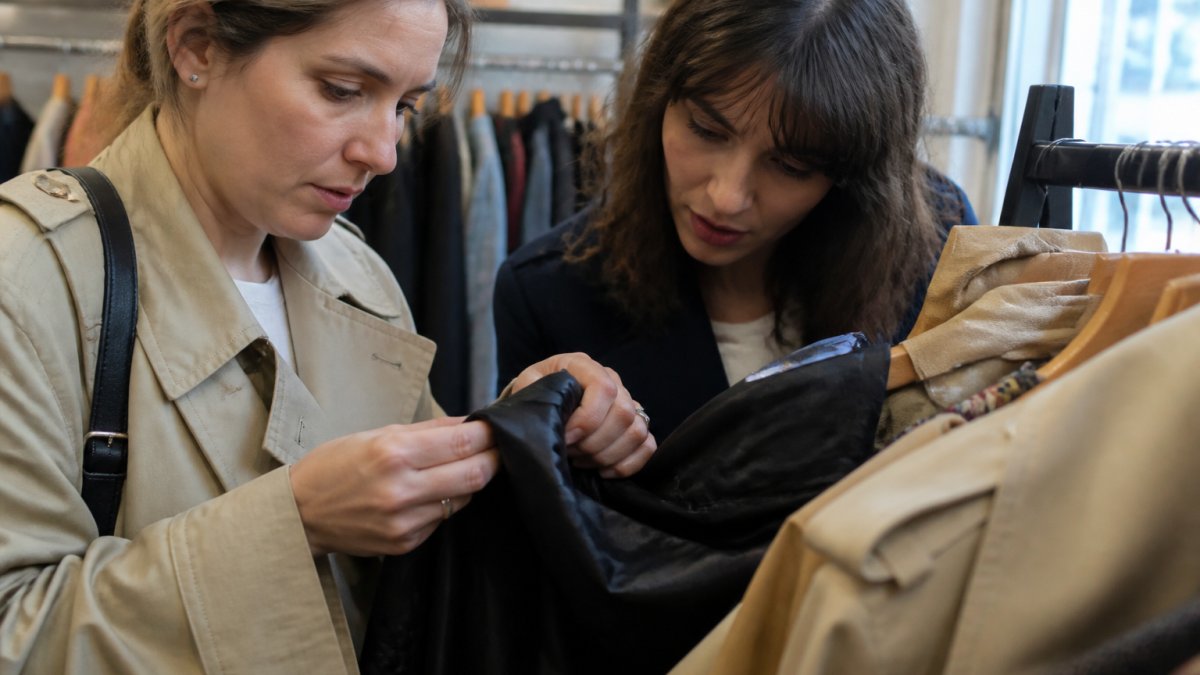 Close-up of hands examining designer garment labels and stitching details on luxury fabric in natural lighting