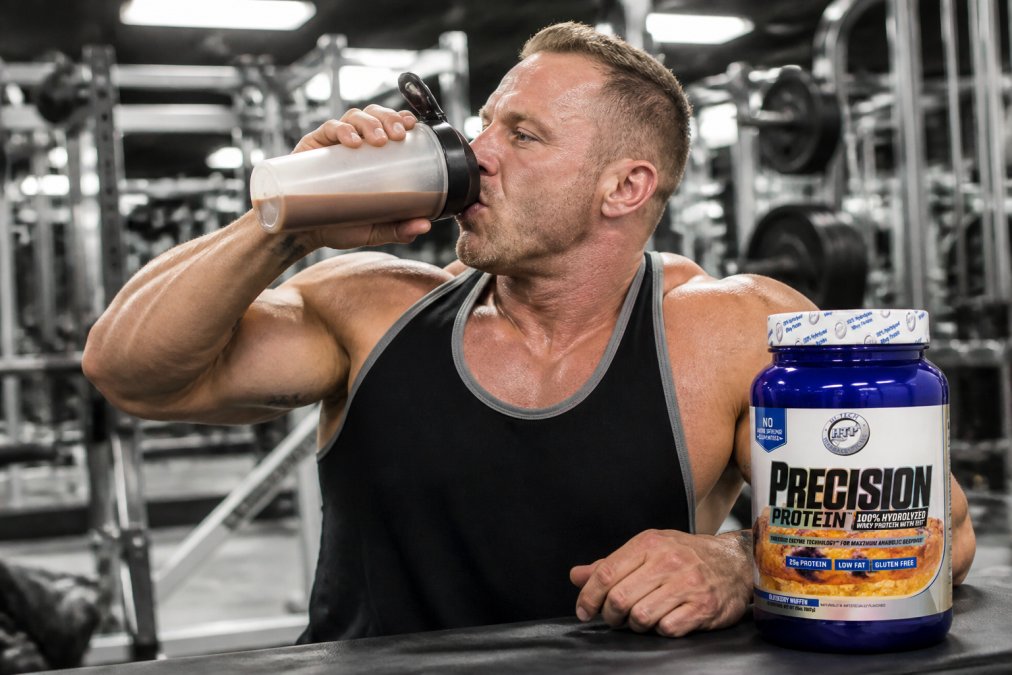 Athlete drinking a protein shake immediately after an intense weightlifting session in a modern gym setting with stainless steel equipment and bright overhead lighting