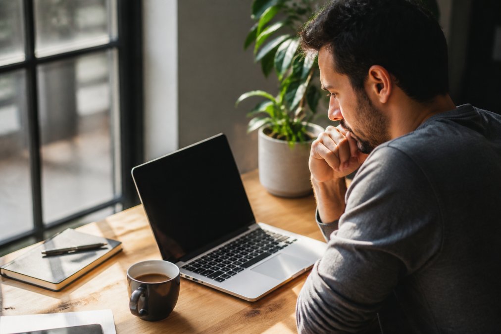 Person checking habit progress on a laptop at a desk with natural morning light, coffee cup nearby, focused expression while reviewing a habit tracking interface