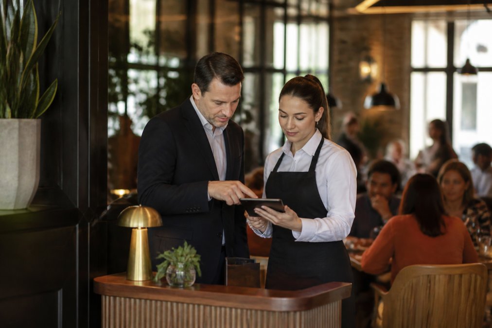 Restaurant manager and server checking a tablet to manage a dining subscription in a bustling restaurant.