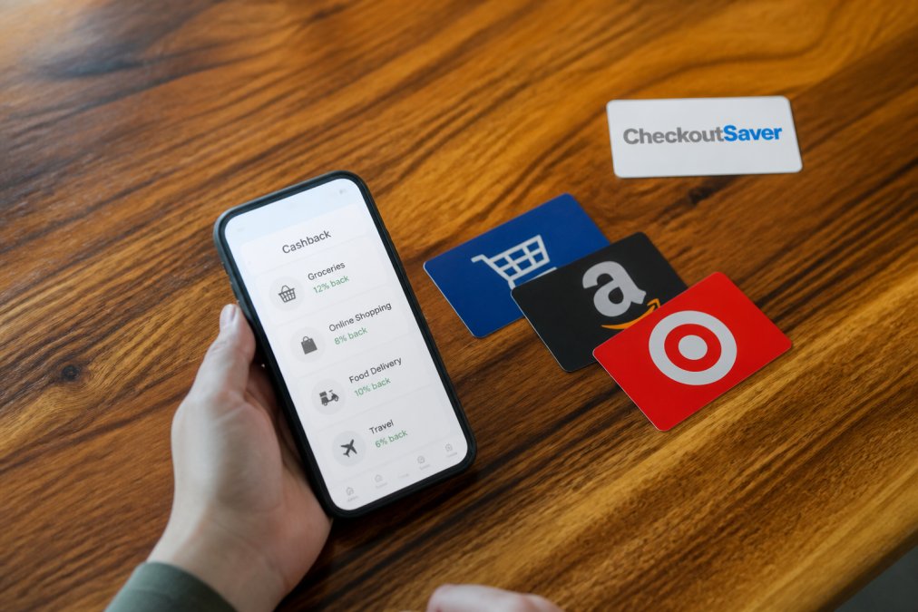 Overhead shot of a person holding a smartphone showing a cashback app next to a stack of retail gift cards on a wooden table