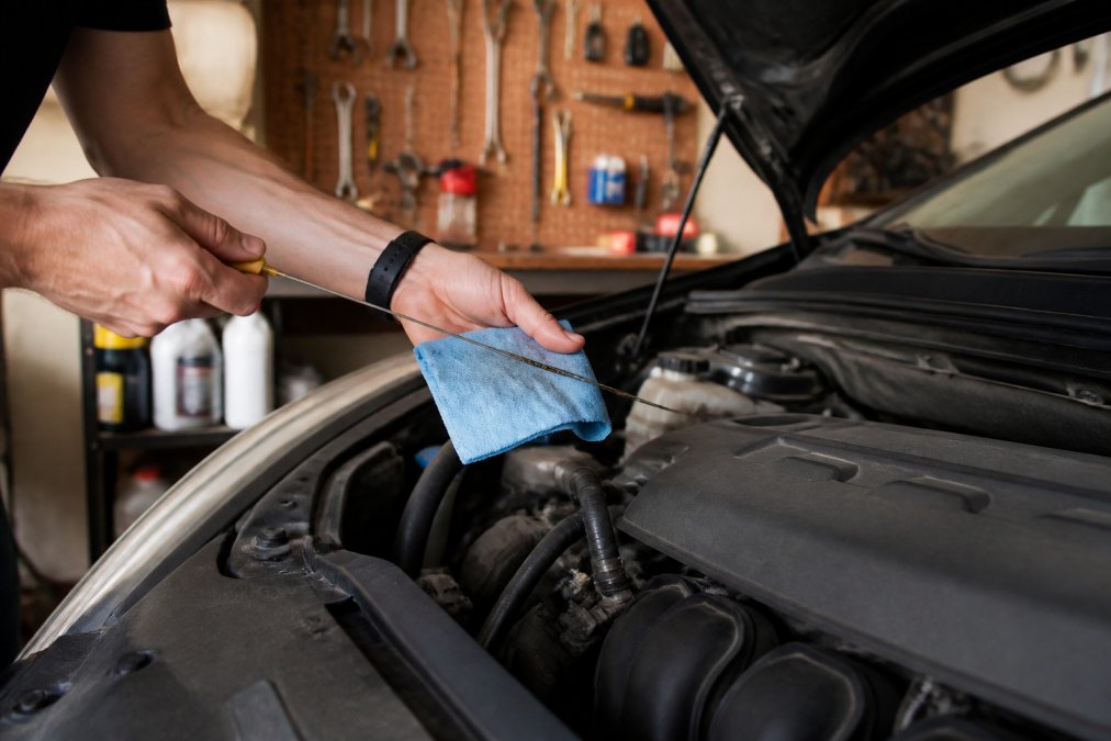 Close-up of a person's hands pulling a clean dipstick from the engine bay to check oil level in a well-lit home garage with tools organized on a pegboard behind