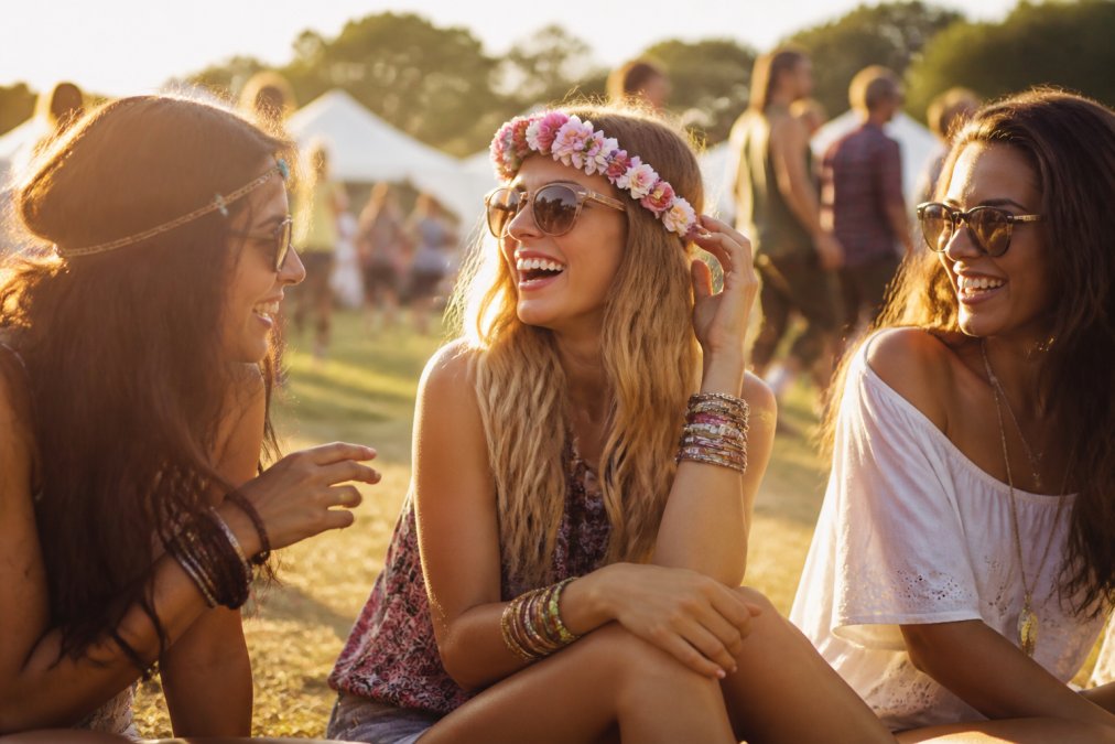 A group of friends at a sunny outdoor festival, one person wearing a colorful flower crown and layered friendship bracelets, laughing together in golden afternoon light