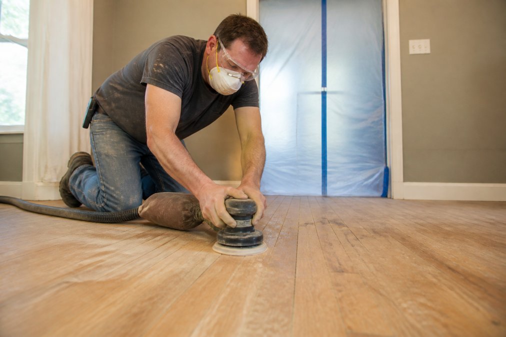 Homeowner using an orbital sander during a hardwood floor restoration project in a home