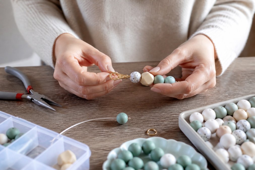 Step-by-step guide for assembling a beaded keychain using pliers and silicone beads on a wooden workspace