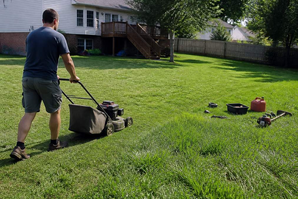 Homeowner pushing a gas mower across a suburban lawn, highlighting the time investment needed for lawn care.