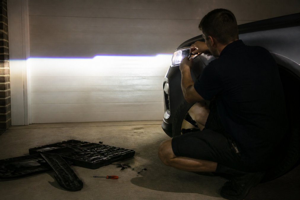 Person using a screwdriver to adjust the aim of aftermarket LED headlights against a garage wall at night