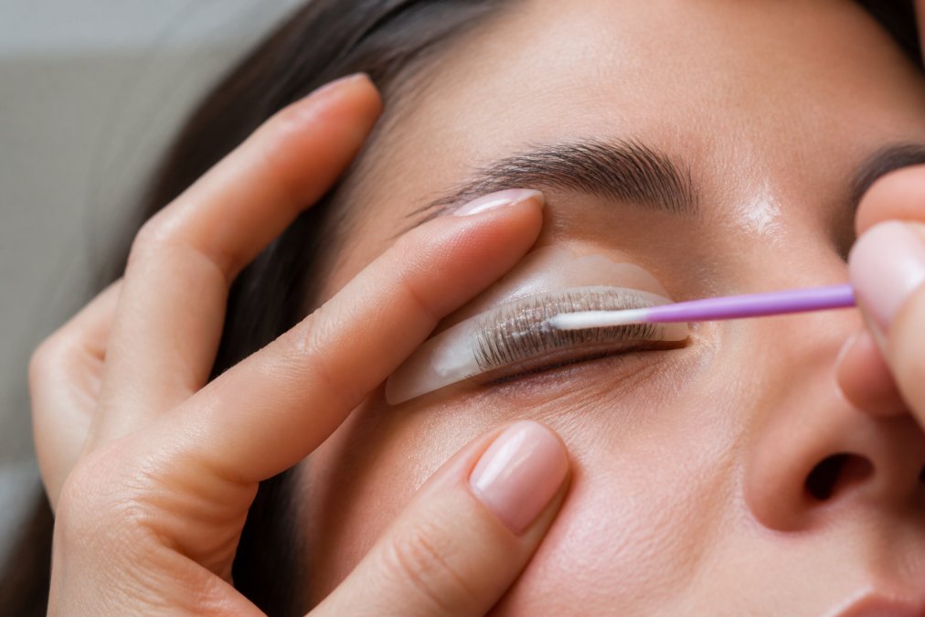 Close-up of a woman's eye during lash lift application, showing silicone rod placement with lifting solution being carefully applied to the lashes with a microbrush