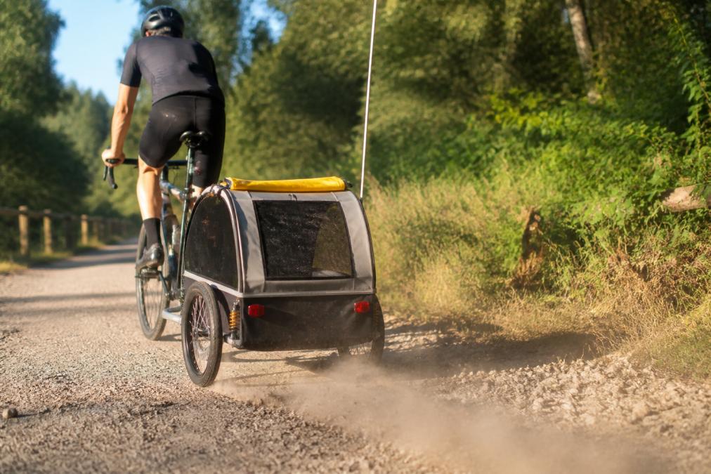 Cyclist towing a trailer with bike trailer shocks over a dusty gravel trail on a sunny day