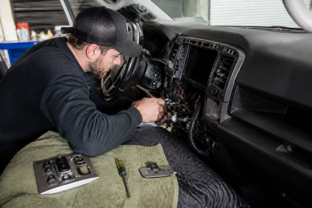 Professional technician installing billet interior trim on a truck dashboard, carefully routing existing wiring away from the new component with precision tools and proper cable management