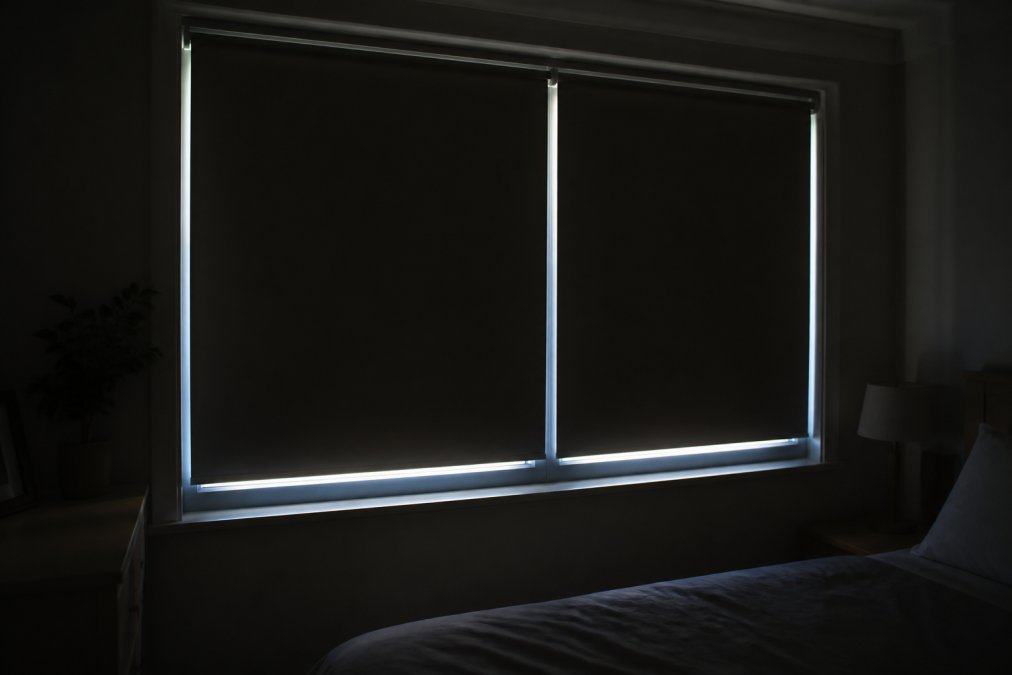 Close-up view of a window at night showing light gaps around the edges of installed blackout blinds, with soft exterior light visible through the gaps