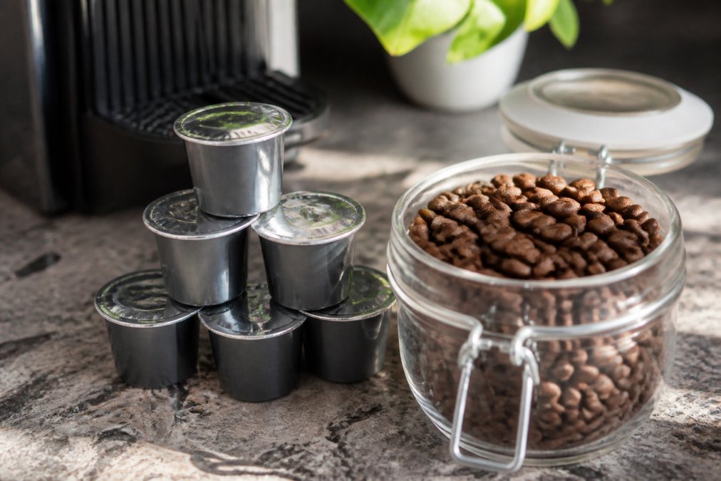 Close-up of nitrogen-sealed coffee pods stacked next to an open container of whole coffee beans, showing the contrast between hermetically sealed and exposed beans in natural light