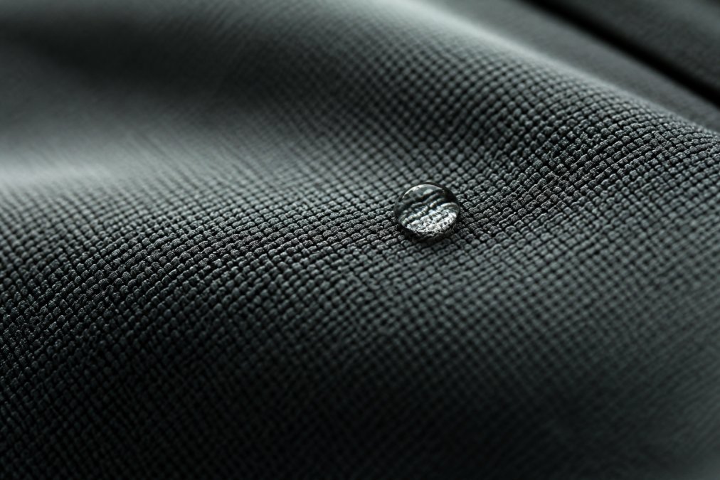 Close-up of compression fabric texture showing the interlocking weave pattern, with a drop of water beading on the surface, macro photography