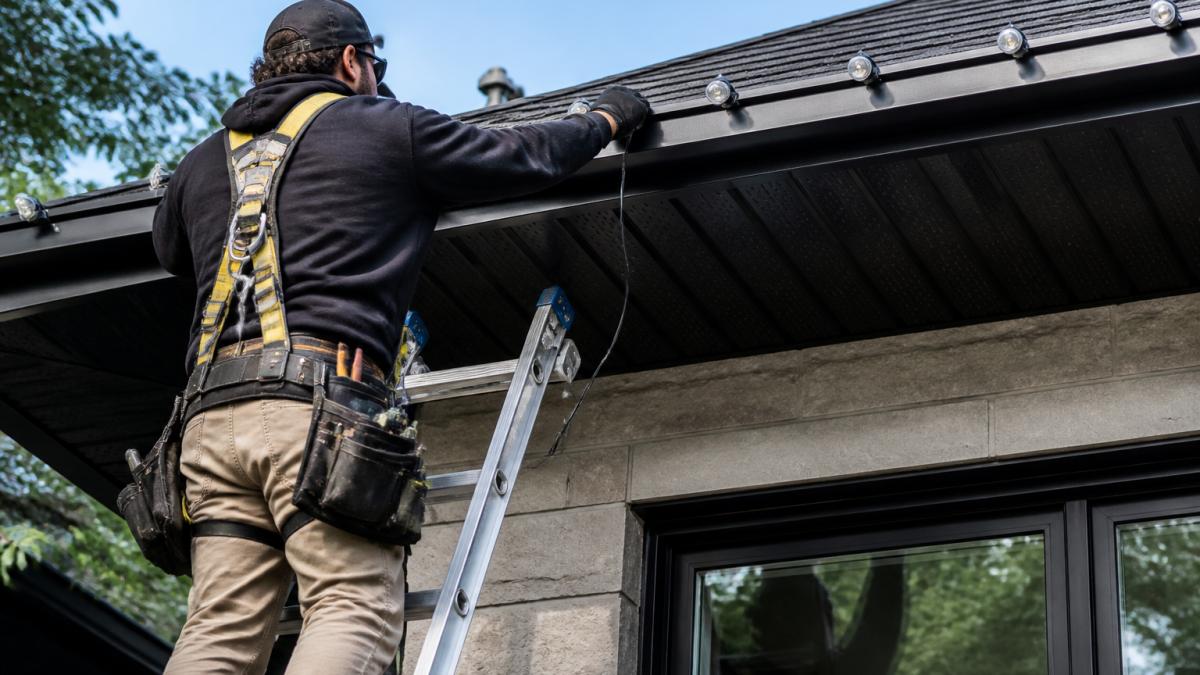 Homeowner wearing a safety harness installing permanent LED roofline lights to see if do permanent lights need professional