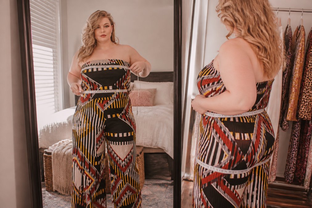 Woman measuring her bust, waist, and hip circumference with a measurement tape in natural light, standing in front of a mirror in a bedroom setting