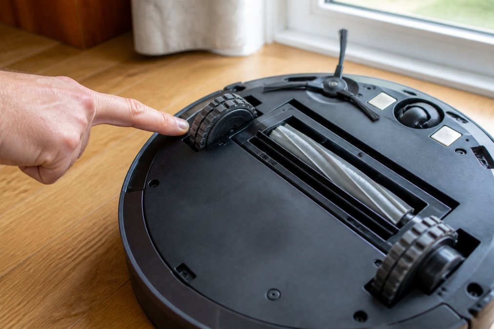Hand pointing to the rubberized wheel and brush roll of a device that can make robot vacuums scratch hardwood floors.