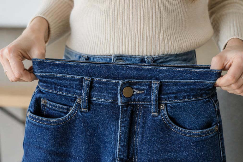 Close-up of a woman's hands stretching the waistband fabric of a pair of high-waisted blue jeans to show the flexibility and give of the material