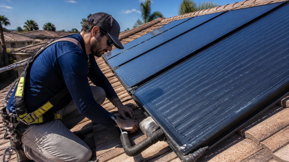 Technician inspecting solar pool heater panels on a roof to see if do solar pool heaters need annual maintenance