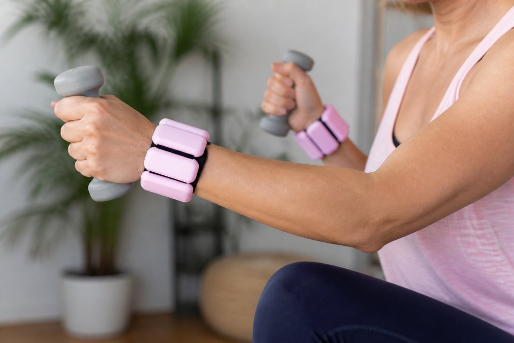 Close-up of a person's wrists and forearms wearing adjustable weighted fitness bands during a controlled arm movement, with hands positioned to show proper grip and wrist alignment, captured in bright indoor lighting