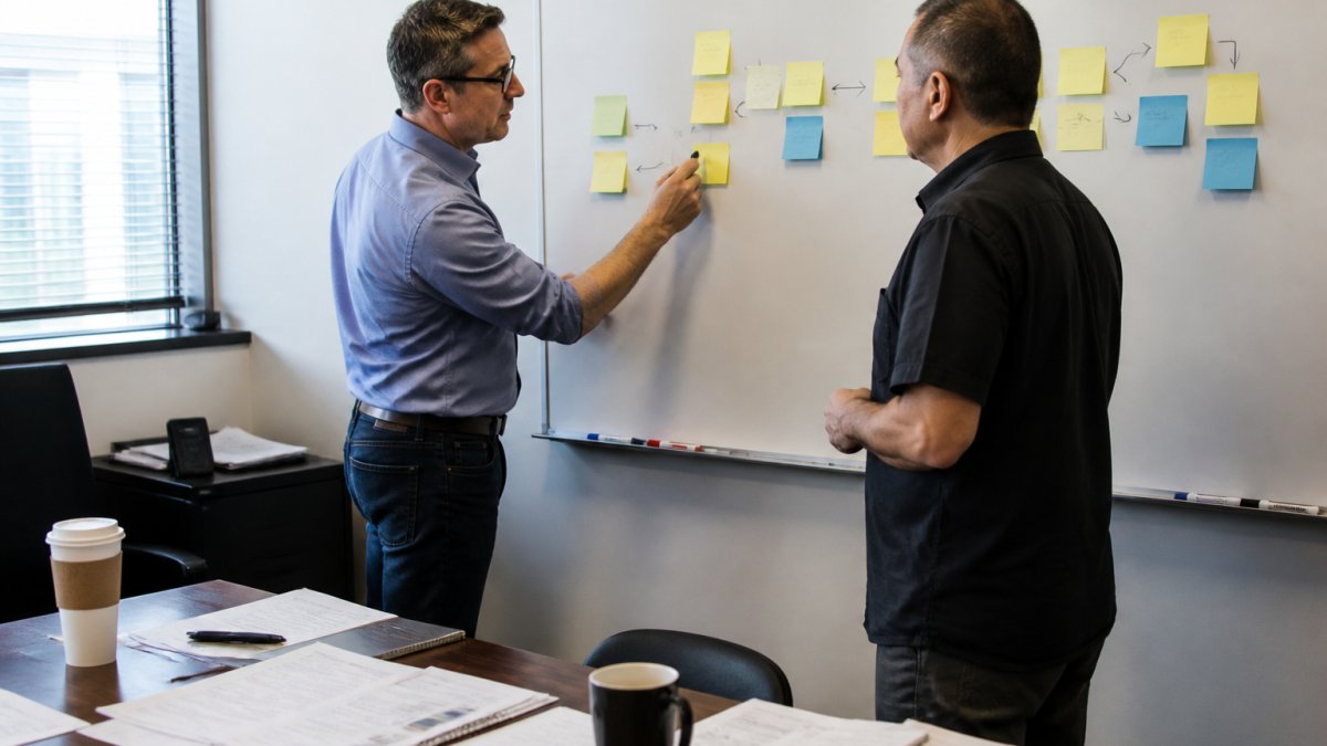 Advisor and business owner mapping a workflow on a whiteboard to identify constraints for an operational turnaround.