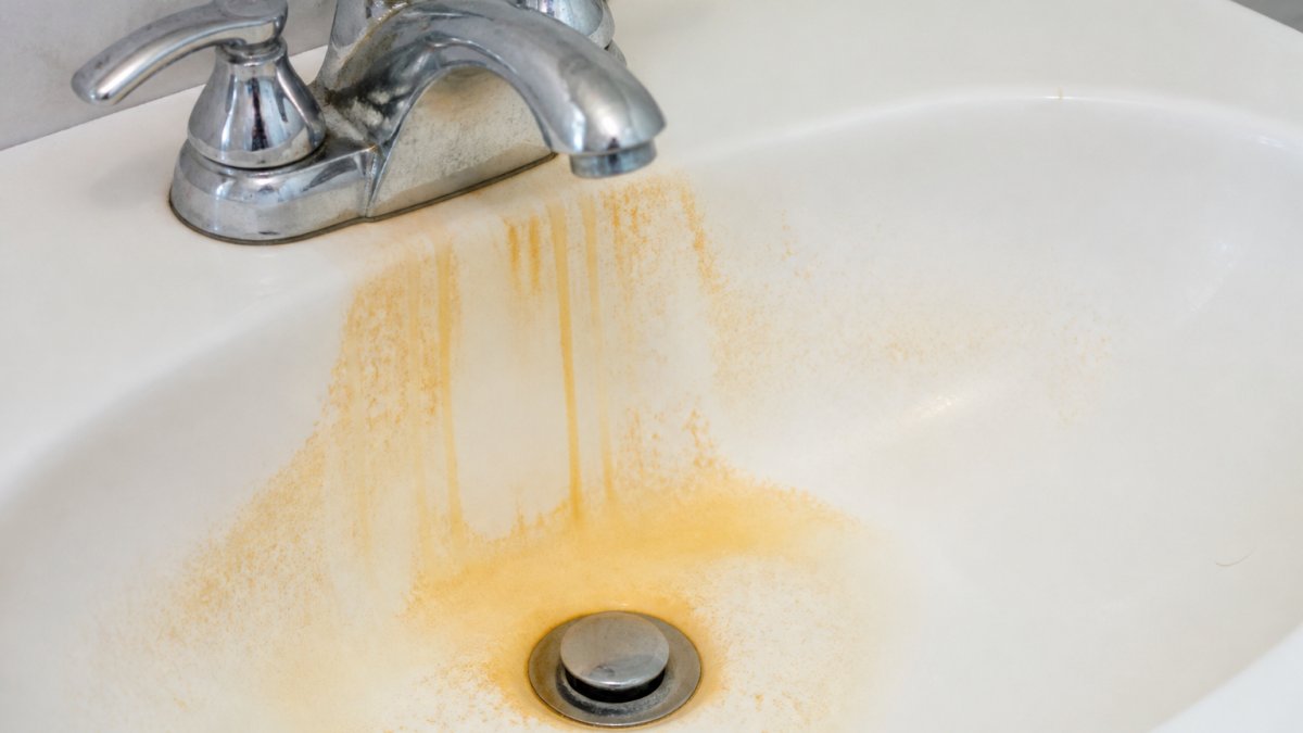 Close-up of orange-brown rust stains on a white bathroom sink or shower fixture, showing the discoloration that remains on fixtures