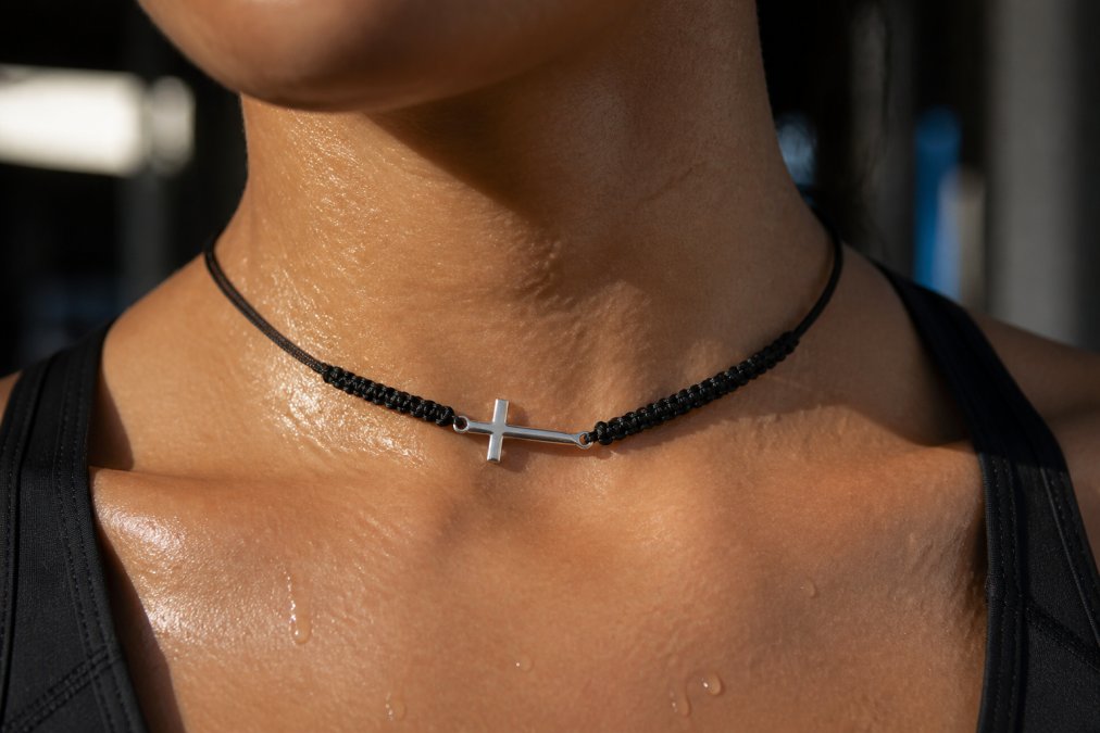 Close-up of a person's neck and collarbone area glistening with sweat after exercise, showing moisture beads on skin where a gold-plated chain would rest, with natural sunlight highlighting the moisture