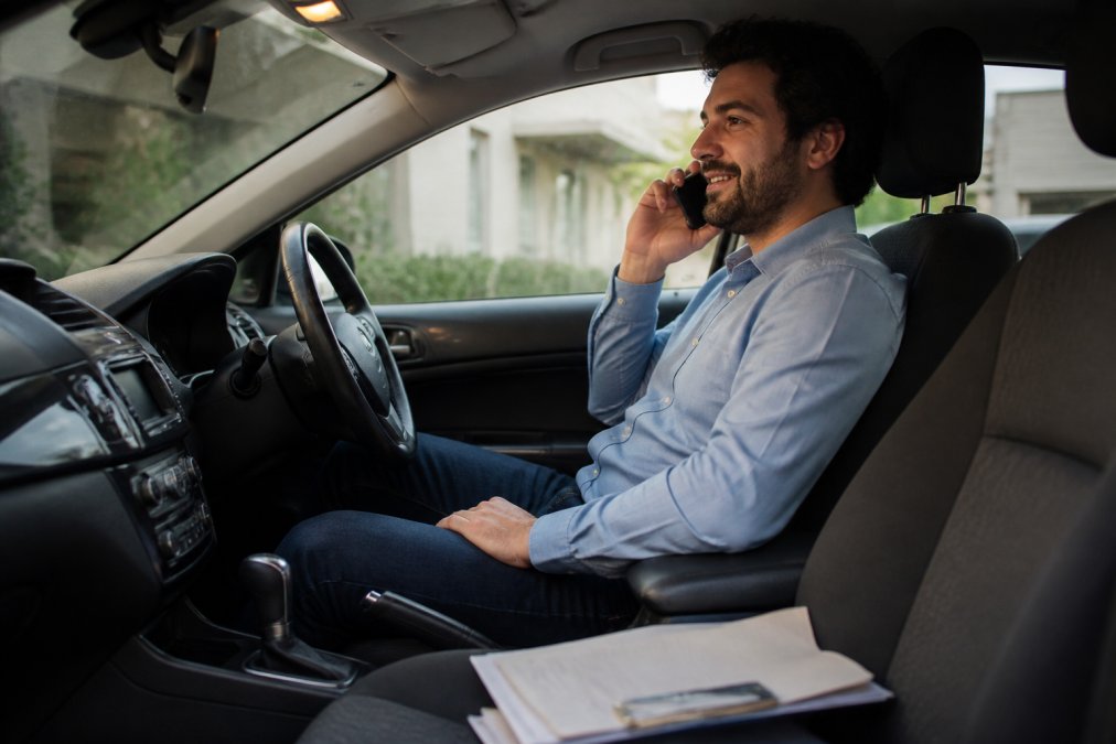 A person sitting in a hire car, relaxed, with a phone to their ear and paperwork on the passenger seat, warm interior lighting suggesting calm and organisation after a stressful event