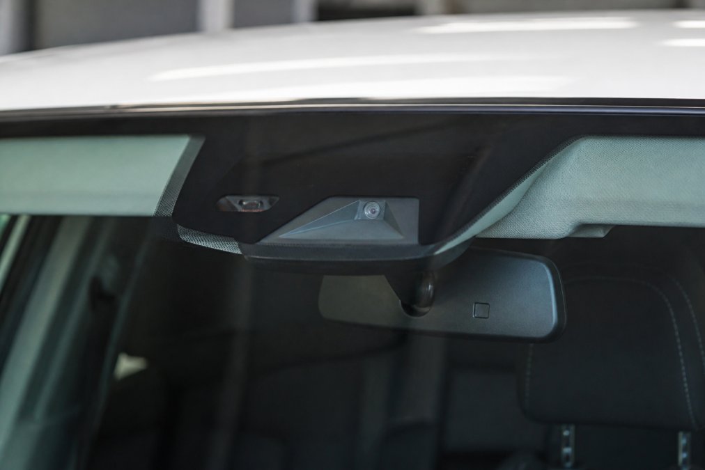 Close-up of a vehicle's windshield with a mounted safety camera sensor visible at the top of the glass, showing the camera's precise alignment position