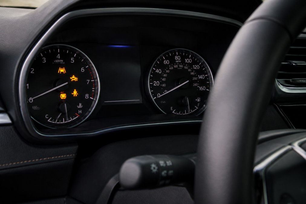 Close-up of vehicle dashboard showing lane departure warning and collision avoidance system icons illuminated on the display with modern instrument cluster
