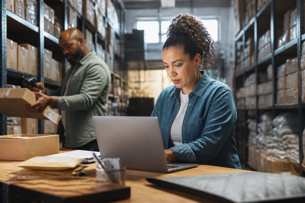 Does Integrated Ecommerce Handle Shipping Inventory Small business owner reviewing real-time inventory levels on a laptop screen while physically checking product stock on warehouse shelves under bright overhead lighting