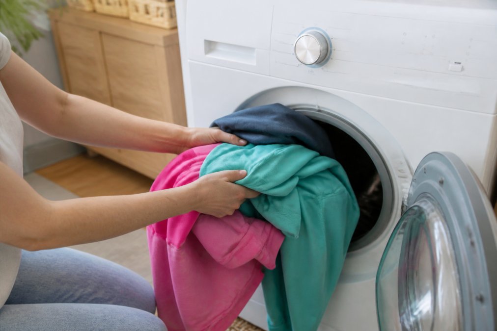 Close-up of hands placing colorful polyester and spandex activewear into a washing machine with the cold water setting visible on the dial
