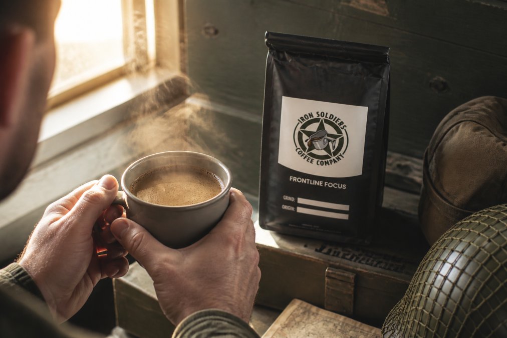 Close-up of a steaming mug of dark mushroom coffee with rich crema, held by hands in soft morning light streaming through a window, showing the beverage's deep brown color and aromatic steam