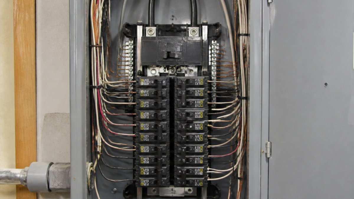 Close-up of an open residential electrical panel showing the main breaker at the top, multiple circuit breakers arranged in rows, and labeled wiring connected to the bus bars inside the metal enclosure