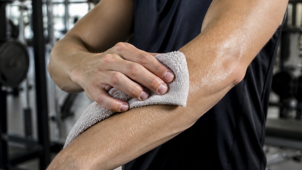 Close-up of a person's forearm wiping sweat with a cotton towel in a gym setting, showing visible moisture on the skin and fabric