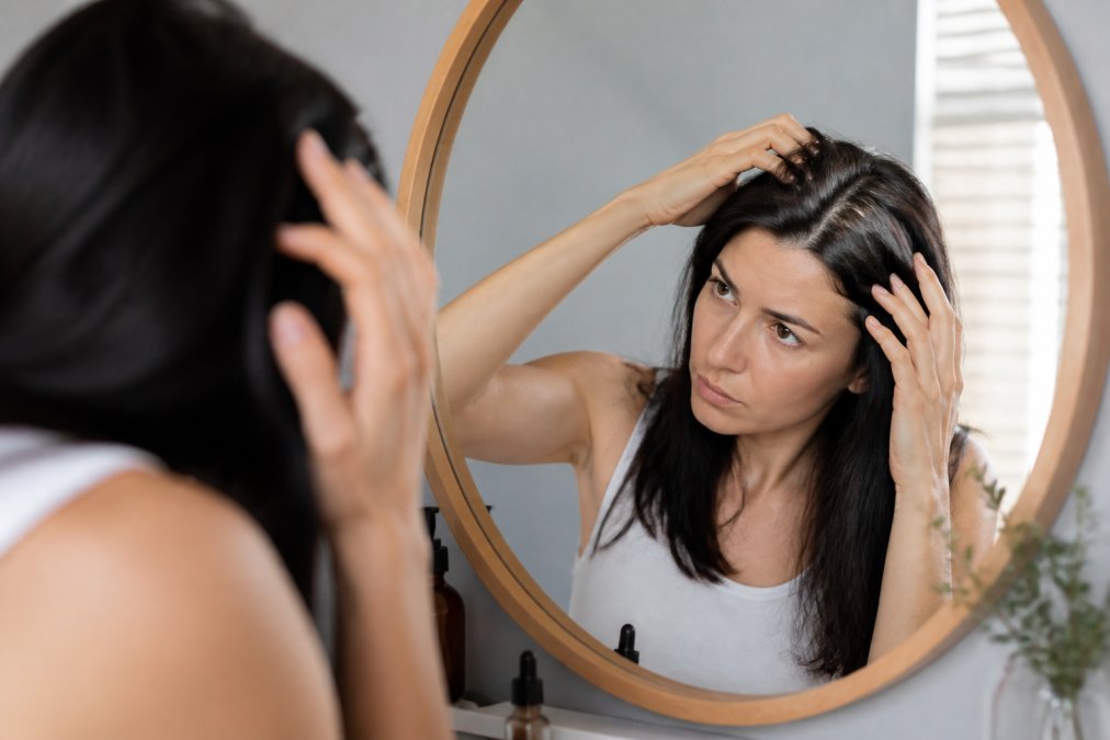 Person examining their hair and scalp in a mirror with a thoughtful expression, depicting the monitoring process during hair growth cycles