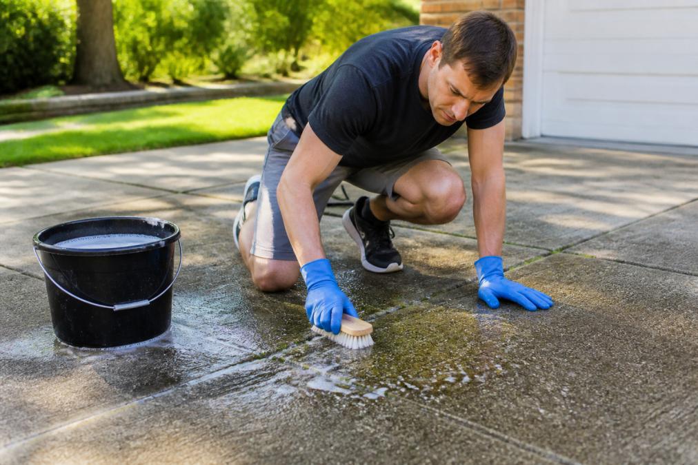 Homeowner scrubbing mold from a concrete driveway to see if pressure washing kills driveway mold effectively.