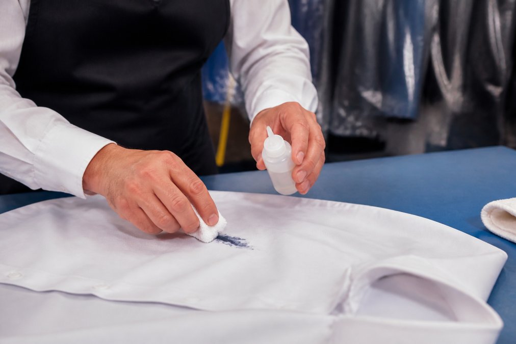 Professional dry cleaner's hands carefully blotting an ink stain on a white dress shirt using specialized solvent and white cloth on a work station