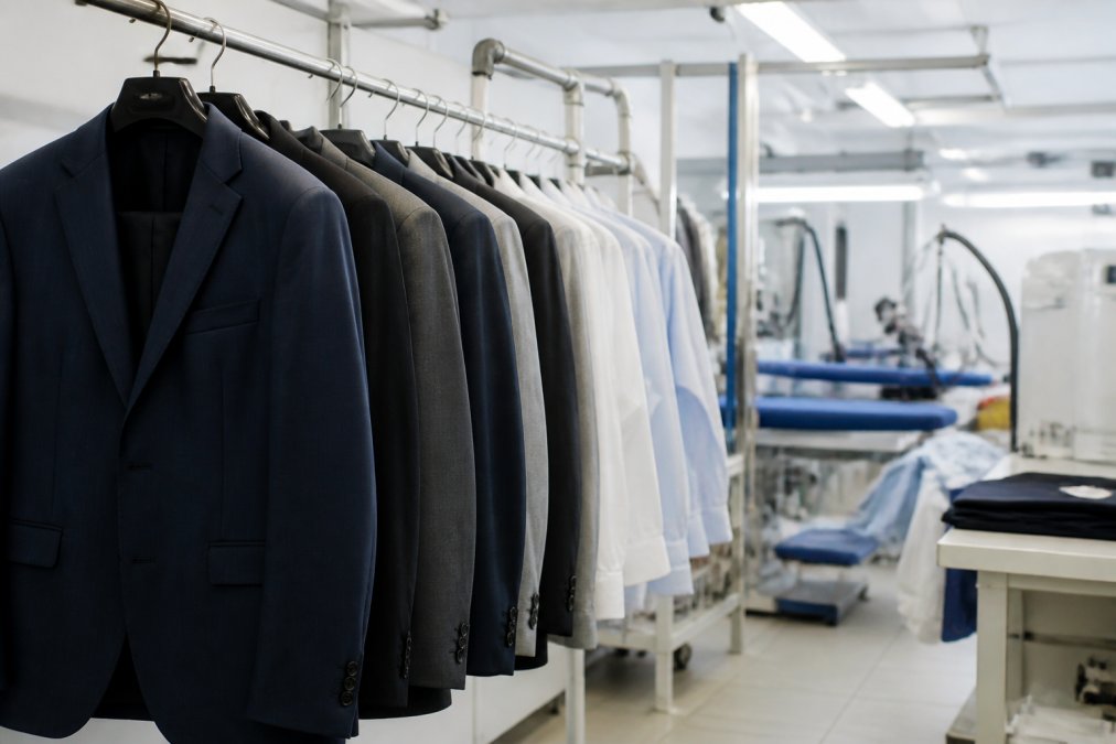 Professional dry cleaning facility with formal blazers and dress garments hanging on racks, showing professional-grade equipment and organized workspace with proper lighting
