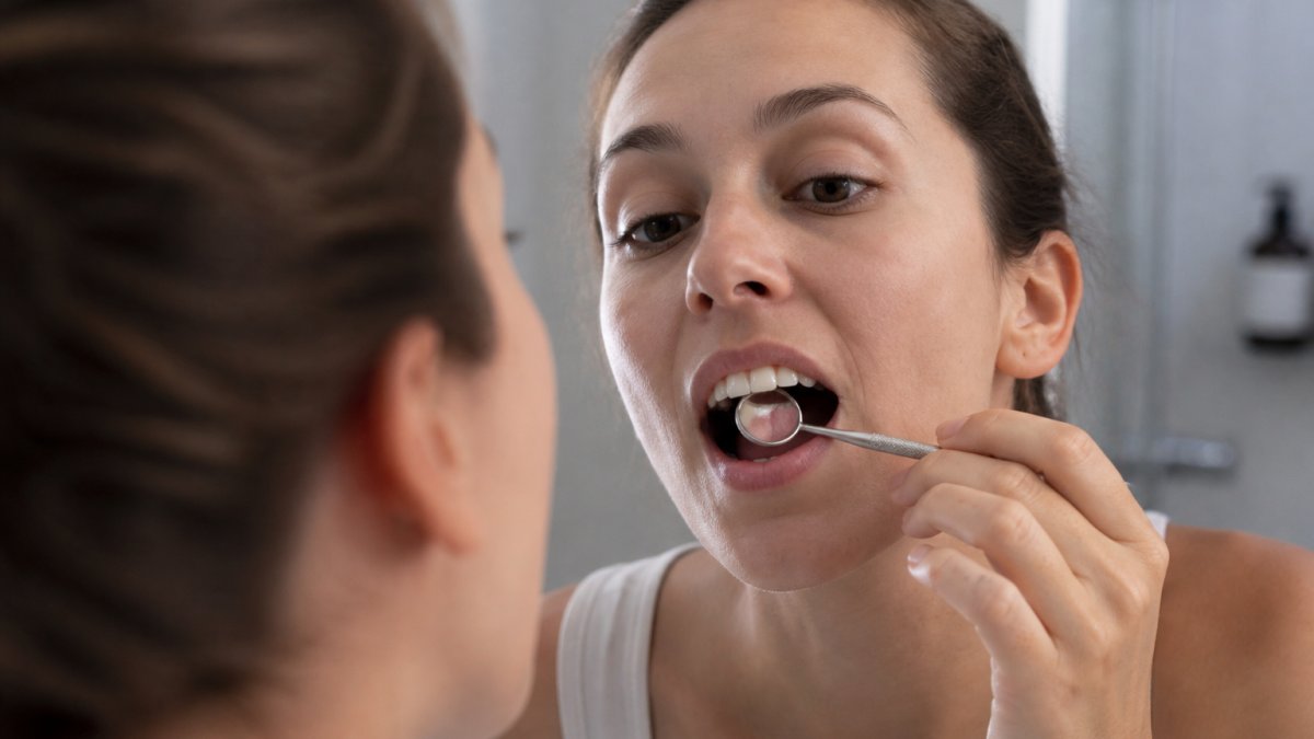 Close-up of a person examining their teeth in a bathroom mirror, holding a small dental mirror, with soft natural lighting highlighting the tooth surface