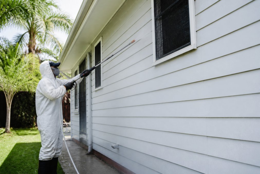 Technician using a gentle soft wash wand on a weatherboard house to show how soft washing protects house paint
