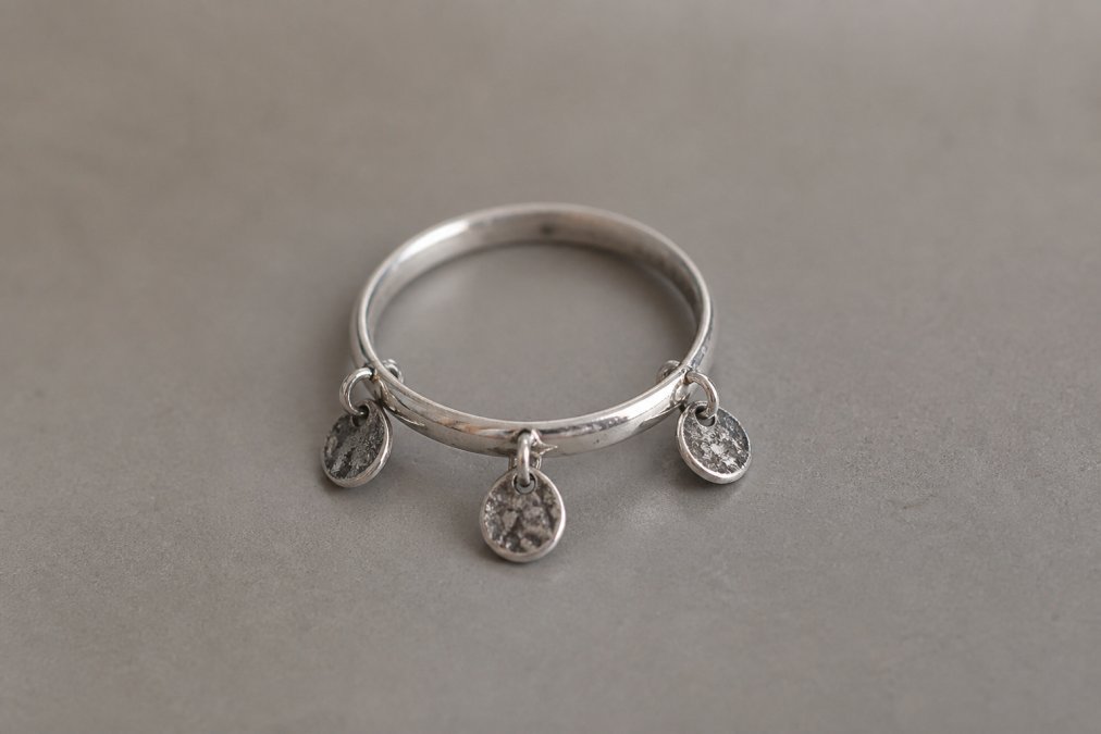 Close-up of a tarnished sterling silver ring showing dark oxidation and discolouration on the band, resting on a neutral grey surface with soft natural lighting