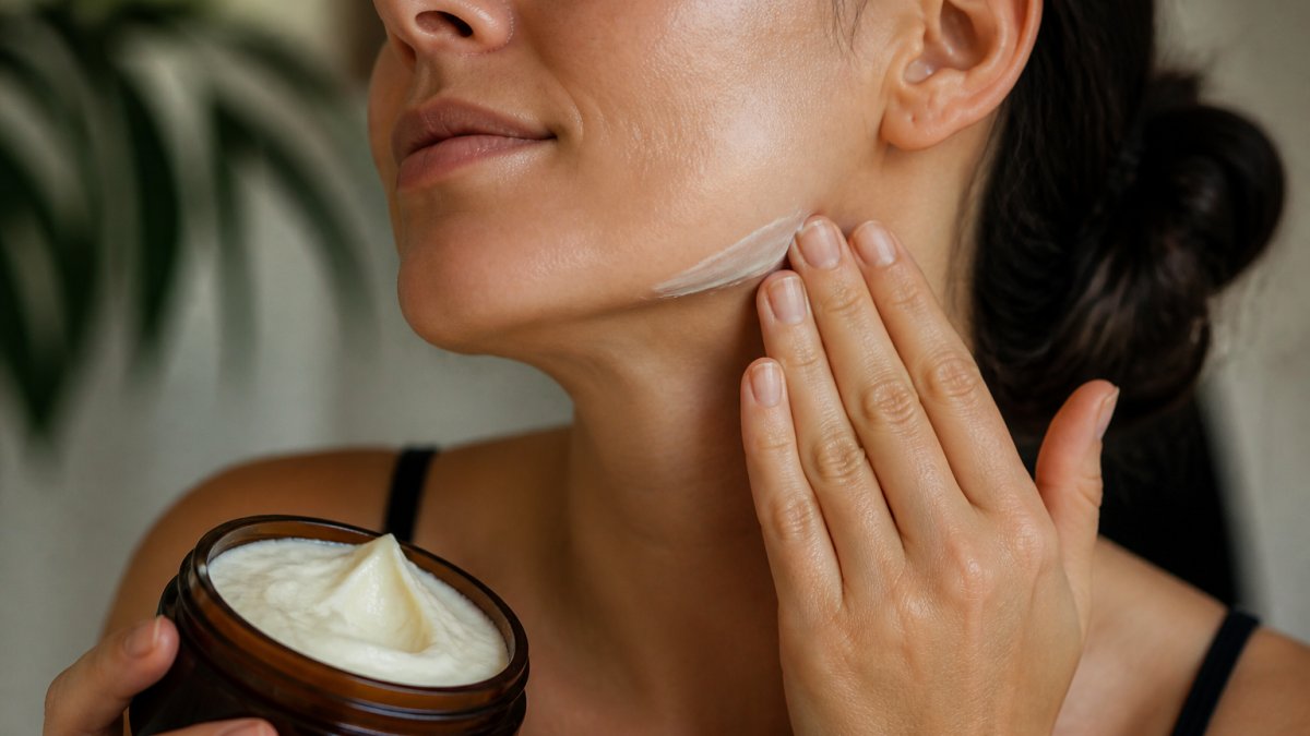 Close-up of a person's hand holding a creamy tallow balm, showing the texture and how it absorbs into the skin on the face or neck