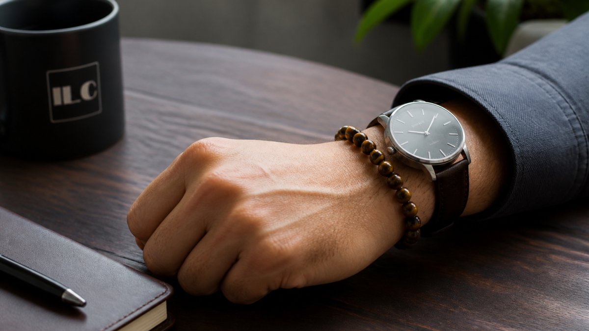 Tiger eye beaded bracelet and leather watch on a wooden desk with coffee and a notebook