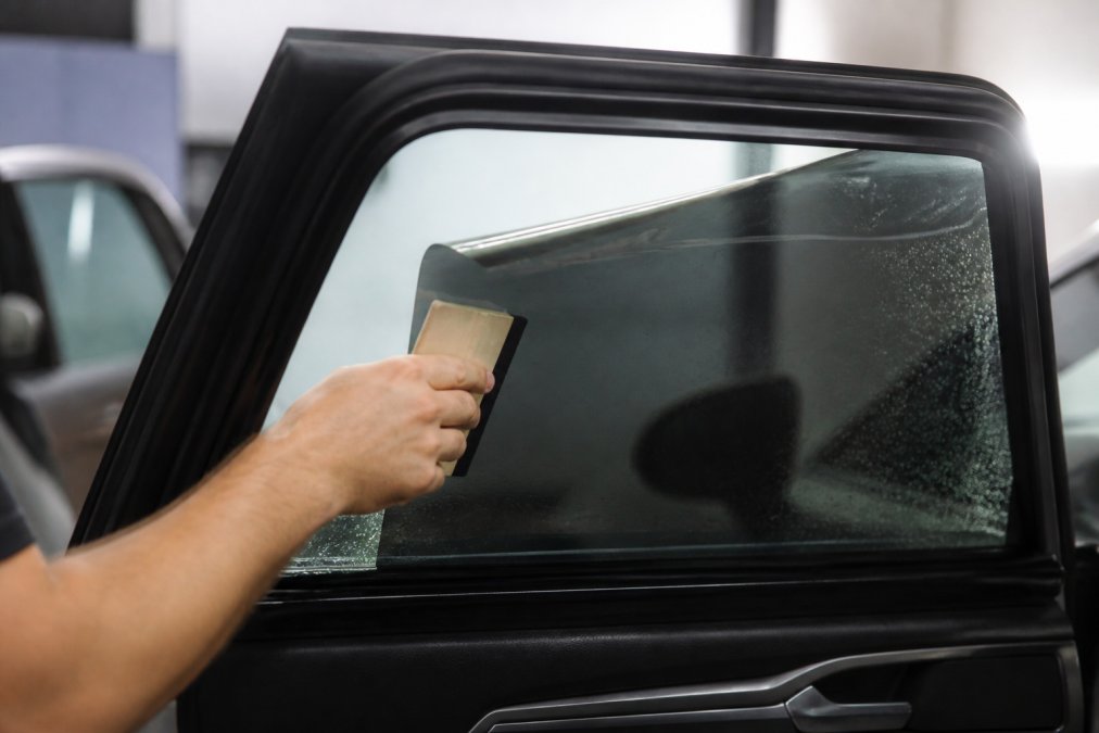 Close-up of a professional installer applying window film to a car side window with a squeegee, showing the film layer clearly
