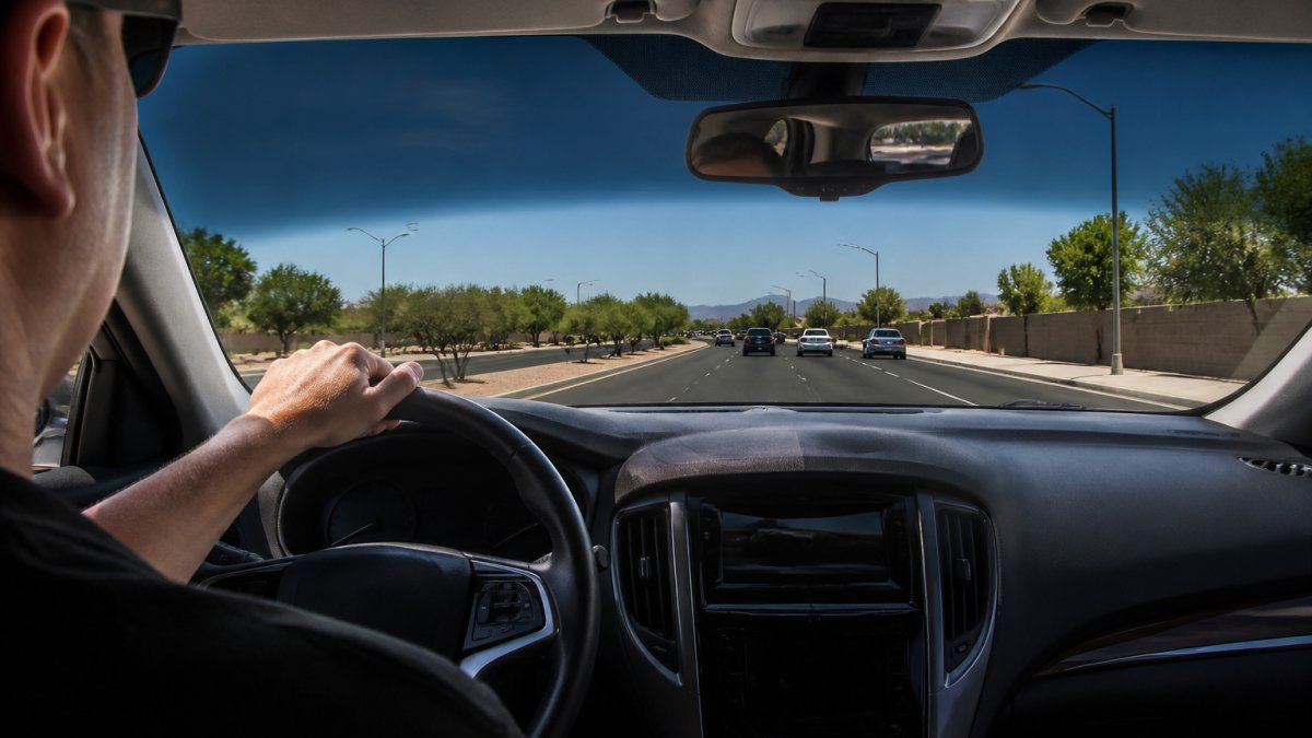 Driver in a sunny car interior with tinted windows showing reduced glare on the dashboard and windshield during bright daytime conditions, with clear visibility of the road ahead