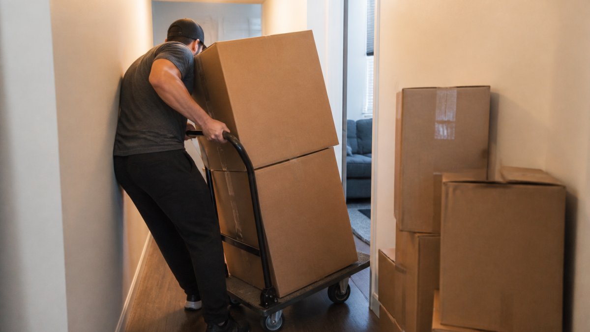 A person struggling to maneuver a large platform dolly through a narrow hallway during apartment moves.