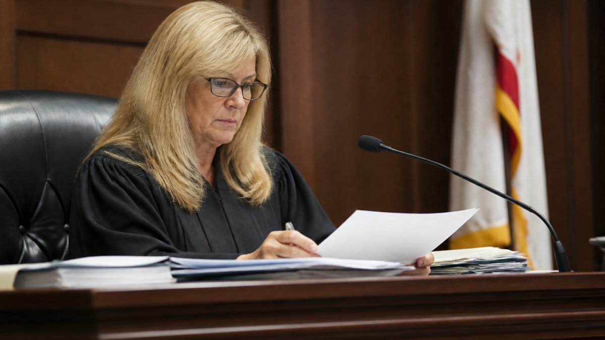 Family law judge reviewing case documents and evidence files at the bench with focused attention during a custody hearing in a formal courtroom