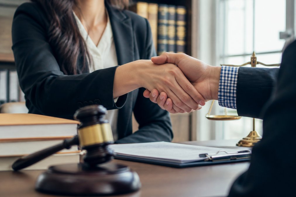 Close-up of hands shaking between an attorney in professional attire and a client in modern office setting, symbolizing trust and legal partnership with warm natural lighting